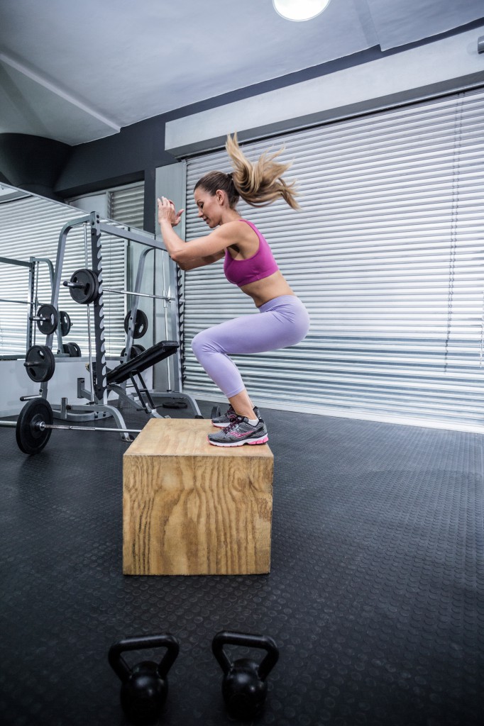 Muscular woman doing jumping squats on a wooden box